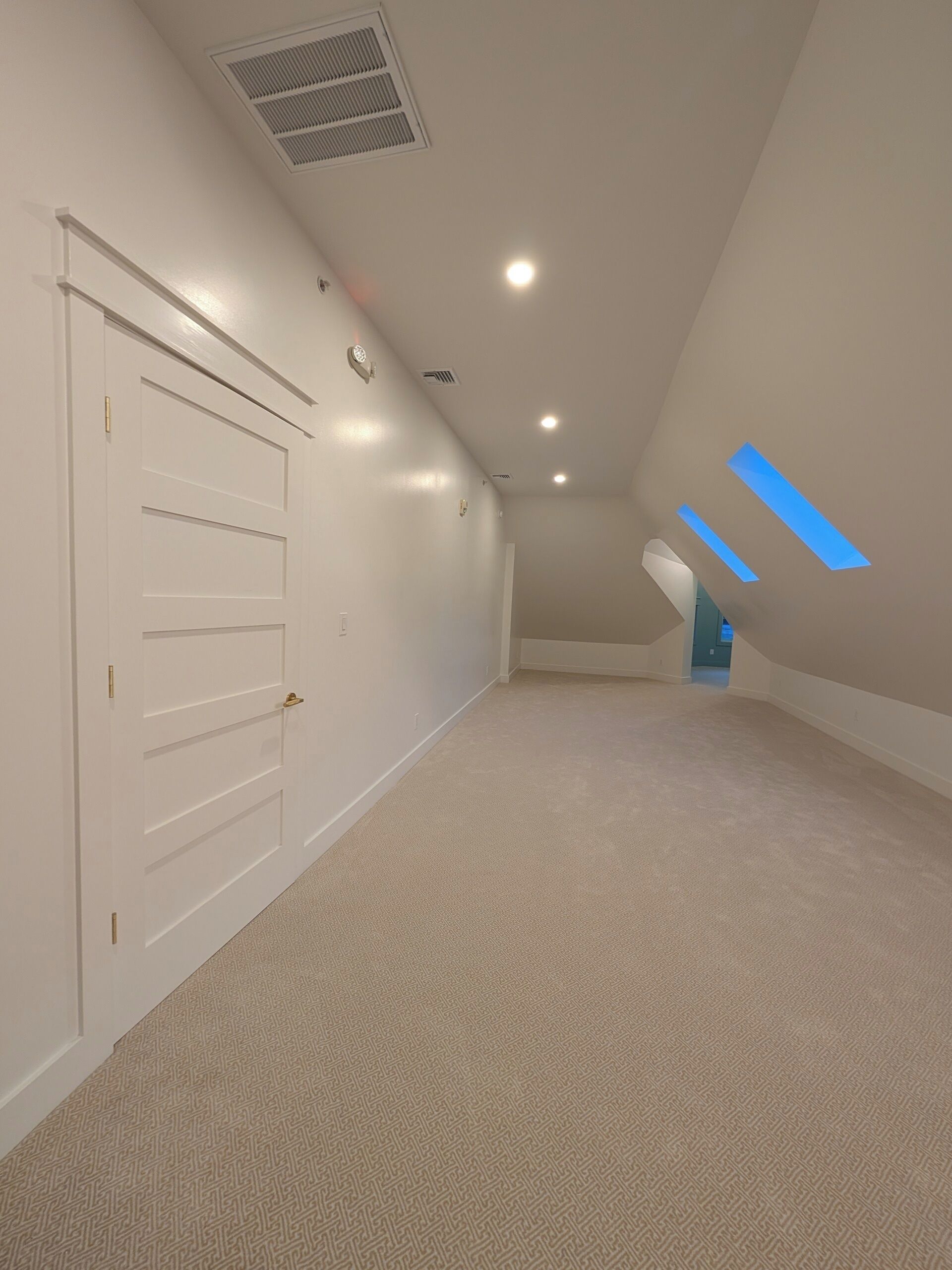 A spacious attic room with a sloped ceiling, a white door with a handle, and a patterned carpet.