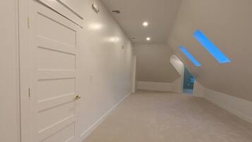 A spacious attic room with a sloped ceiling, a white door with a handle, and a patterned carpet.
