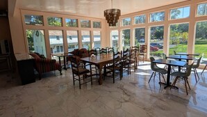Un vaste espace dédié à la salle à manger, avec une grande table et des chaises, entouré de grandes fenêtres offrant une vue sur un quartier résidentiel.