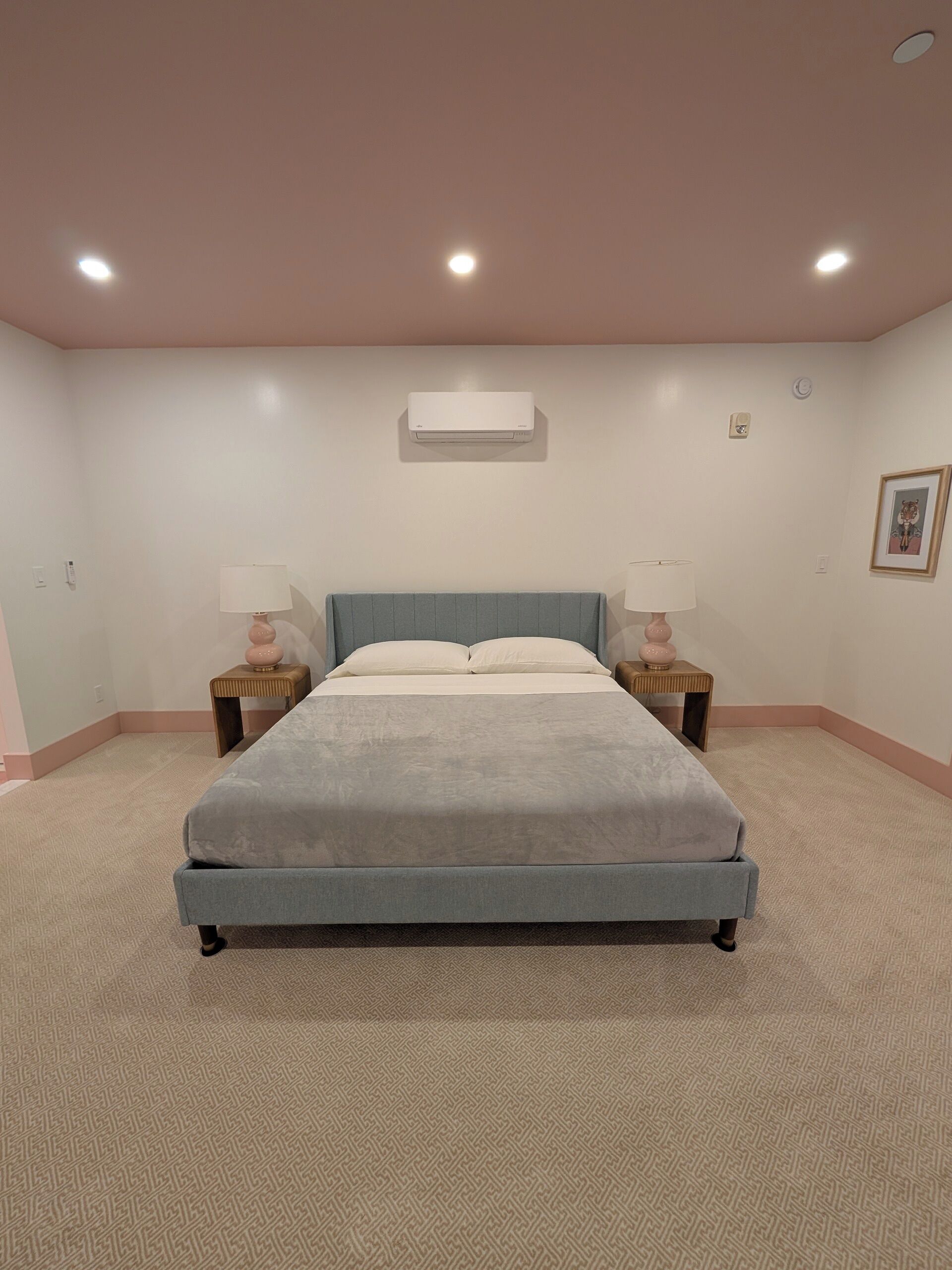 Un dormitorio con una cama grande, dos mesitas de noche con lámparas, una lámpara de techo y un aire acondicionado de pared.