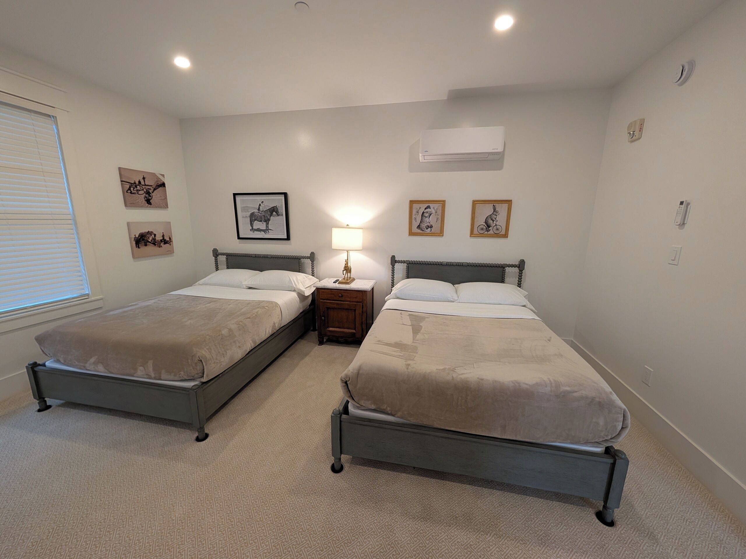 A bedroom with two single beds, a bedside table with a lamp, and wall-mounted air conditioning.