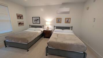 A bedroom with two single beds, a bedside table with a lamp, and wall-mounted air conditioning.