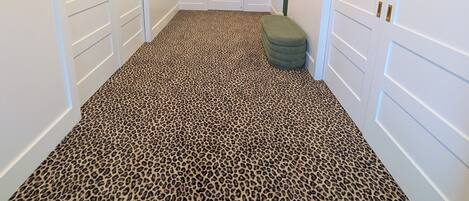 A hallway with white doors, a leopard print carpet, and a green bench.