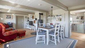En rummelig opholdsstue med spisebord, hvide stole, en rød sofa og et køkken med moderne hårde hvidevarer.