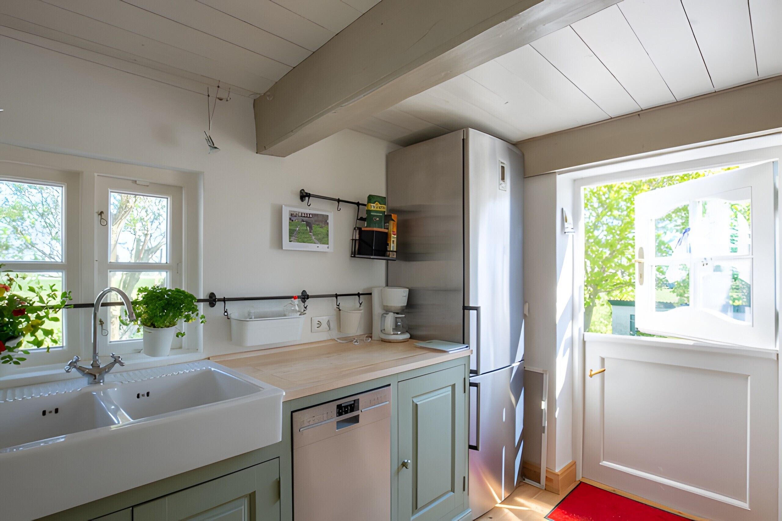 Una cocina con lavamanos, lavavajillas, refrigerador y ventana con vista a la vegetación.