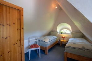 Un dormitorio de ático pequeño y triangular con puerta de madera, cama individual, silla, mesita de noche y ventana con una planta.