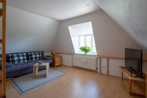 Ein geräumiger Loft mit hoher Decke, einem großen Fenster mit Blick, einem dunkelblauen Sofa, einem Holztisch und einem Fernseher auf einem Holzständer.