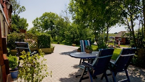 Een terras met buitenmeubels, een ronde tafel en plantenpotten.