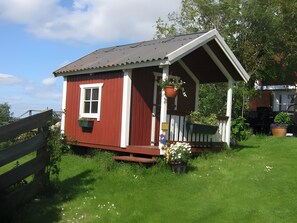 A small red wooden house with a porch, a window, and a door. - Apartment 'Fewo Appelhof Ingrid Marie' with Private Terrace, Shared Garden and Wi-Fi (Pellworm)