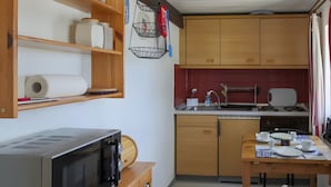 Een compacte keuken met houten kastjes, een magnetron, een spoelbak en een eettafel met stoelen.