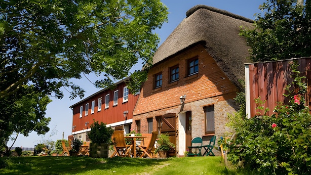 Een traditioneel bakstenen gebouw met een rieten dak, een houten tafel met stoelen, en een tuinpad.