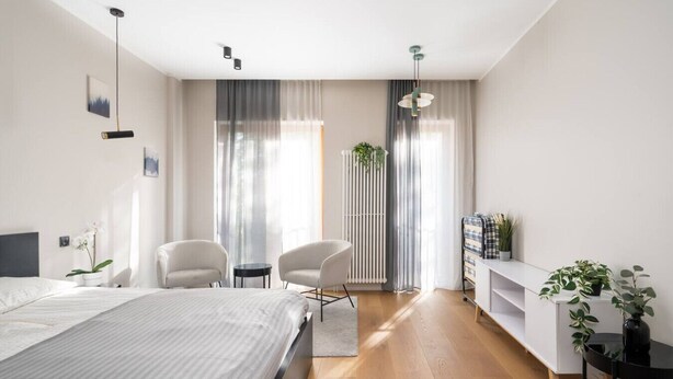 Ein modernes Schlafzimmer mit einem großen Bett, zwei Stühlen, einem kleinen Tisch, einem Heizkörper und einem Regal mit Pflanzen.