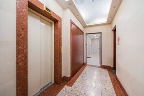 A hallway with marble flooring, a ceiling with recessed lighting, and wooden doors with a number plate. - Modern Old Town Studio – Kungu 25 Apartments (Rīga)