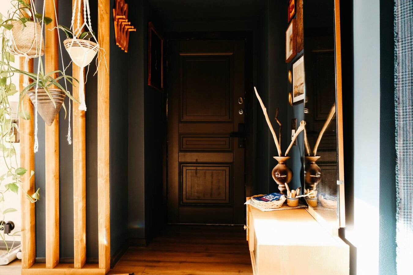 A hallway with wooden flooring, a door at the end, and a table with a vase and wooden sticks.