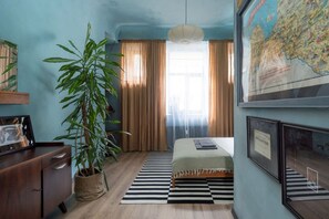 A bedroom with a bed, a map on the wall, a plant, and a desk. - Dark & Moody Mid Century Apartment (Riga)