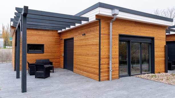 A modern building with wooden paneling, a garage door, and outdoor seating. - House 2: 8 high-quality vacation homes with private sauna & jacuzzi on Sweet Lake (Seegebiet Mansfelder Land)