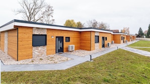 A row of modern buildings with wooden facades and stone accents, featuring a flat roof and a gravel pathway leading to the entrance. - House 2: 8 high-quality vacation homes with private sauna & jacuzzi on Sweet Lake (Seegebiet Mansfelder Land)