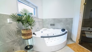 A modern bathroom with a freestanding bathtub, a potted plant, and a small table with a candle. - House 2: 8 high-quality vacation homes with private sauna & jacuzzi on Sweet Lake (Seegebiet Mansfelder Land)