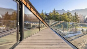 Una terraza de madera con barandas de vidrio que da vista a un paisaje nevado y montañas.