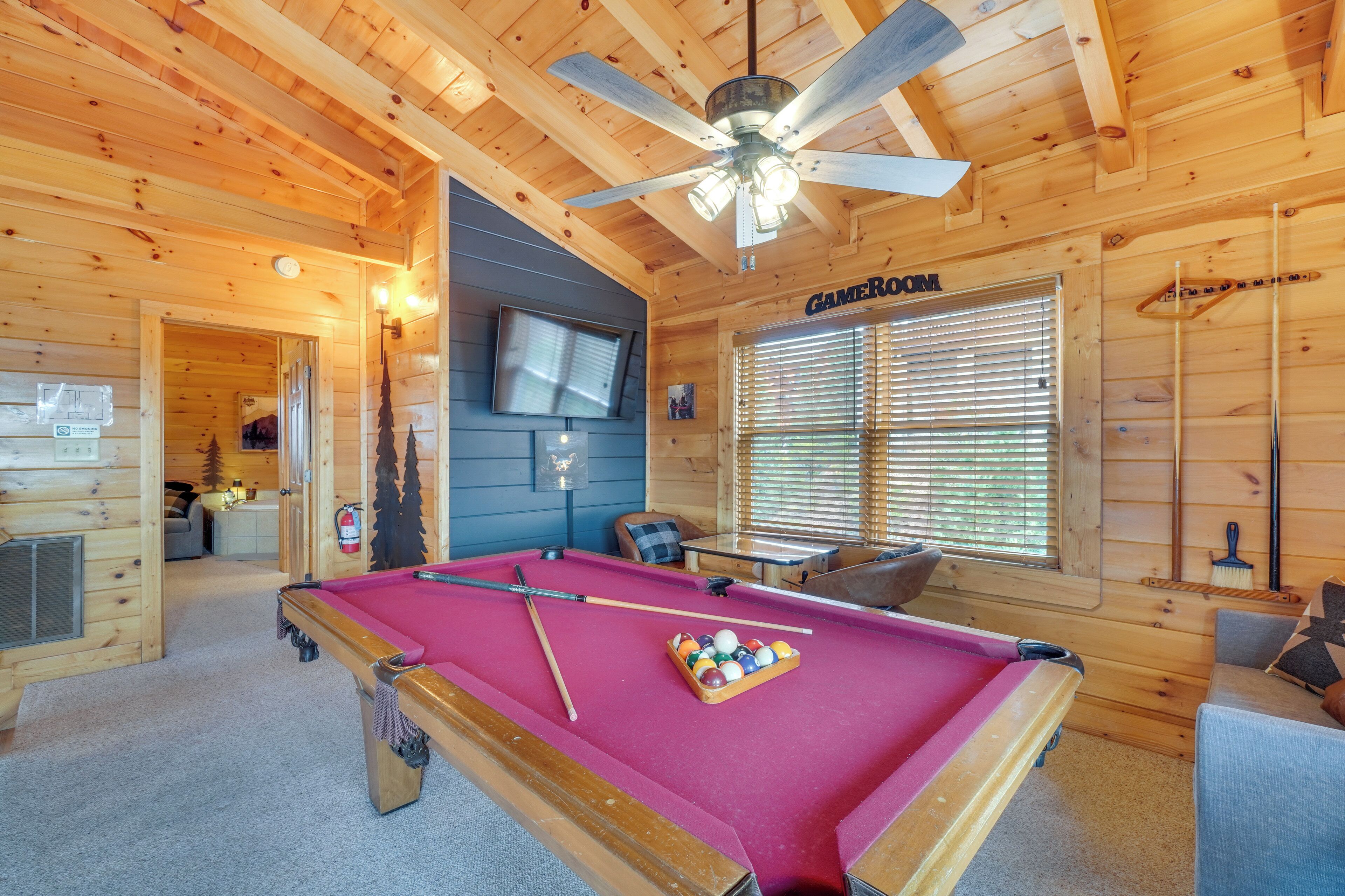 Une cabane en bois équipée d’une table de billard, d’un ventilateur de plafond et d’un téléviseur.