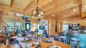 A spacious wooden cabin with a dining area, kitchen, and living room. - Resort-style Smokies Cabin w/ Hot Tub + Game Room (Sevierville)