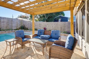 Ein überdachter Patio-Bereich mit Korbmöbeln, einem Pool und einem Holzzaun im Hintergrund.