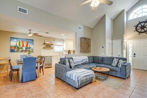 Ein geräumiges Wohnzimmer mit einem grauen Ecksofa, einem Essbereich mit Holztisch und Stühlen sowie einer Küche im Hintergrund.