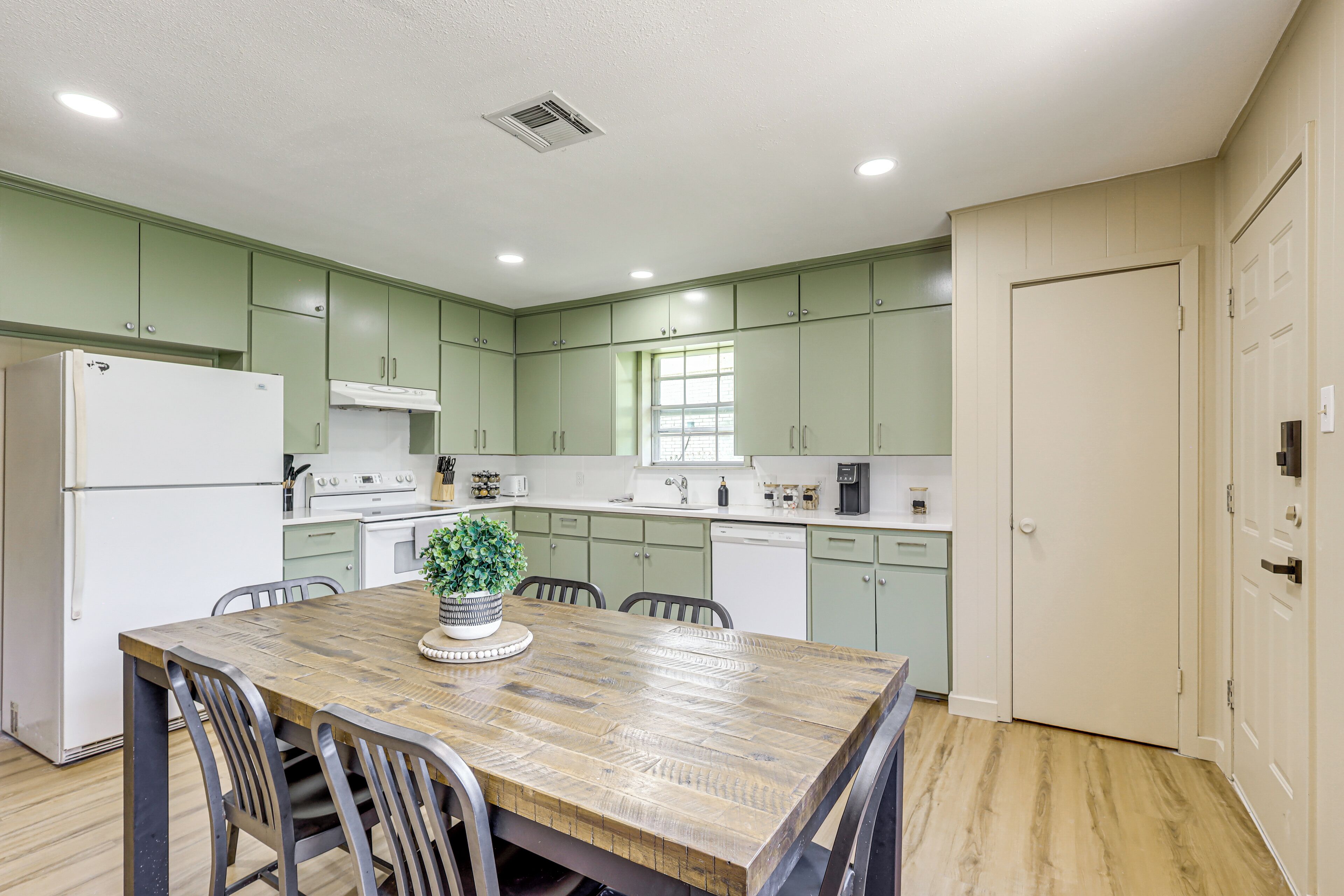 A modern kitchen with green cabinets, a wooden dining table, and a refrigerator.