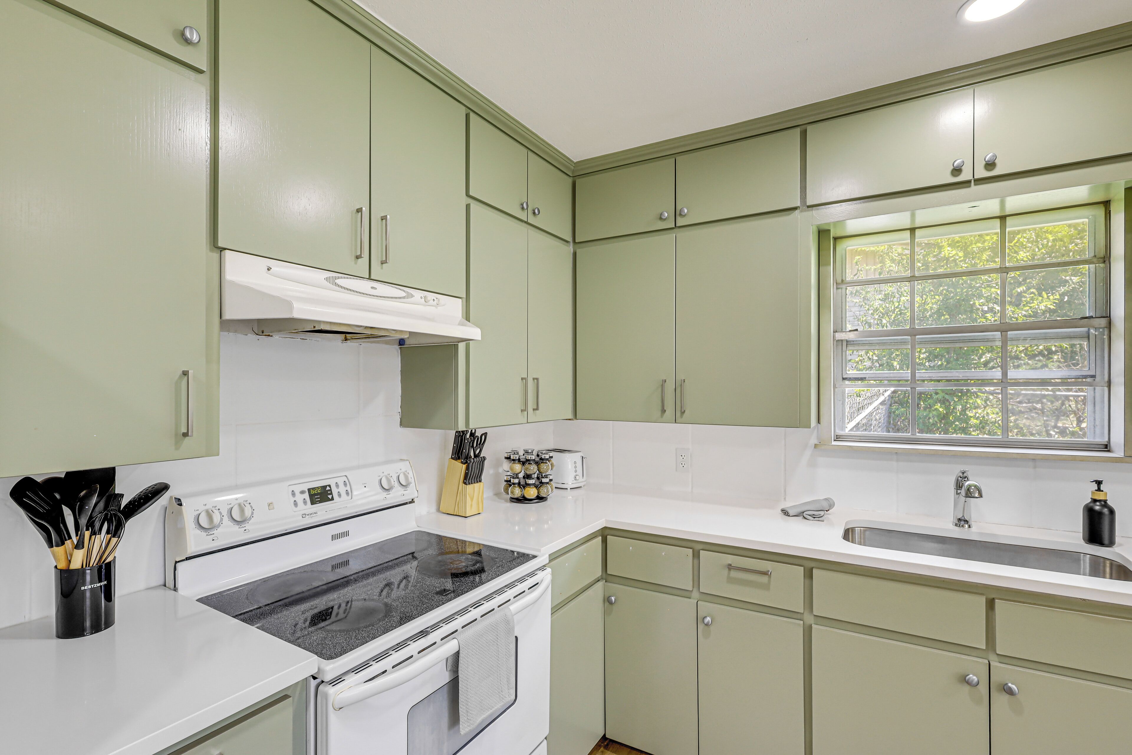 A kitchen with green cabinets, a white stove, and a window with a view of greenery.