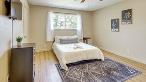 Una camera da letto con un letto, una ventola a soffitto, una finestra con tende, un tavolino e decorazioni alle pareti.