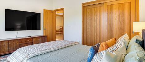 A bedroom with a large bed, a television mounted on the wall, wooden wardrobes, and a door leading to another room.