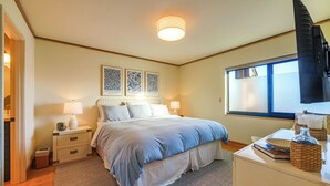 A bedroom with a bed, bedside tables, a desk, and a window. - Stunning Ocean Views! Oregon Coast Condo (Gearhart)
