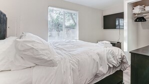 Une chambre à coucher avec un lit, un téléviseur fixé au mur et une fenêtre avec des stores.