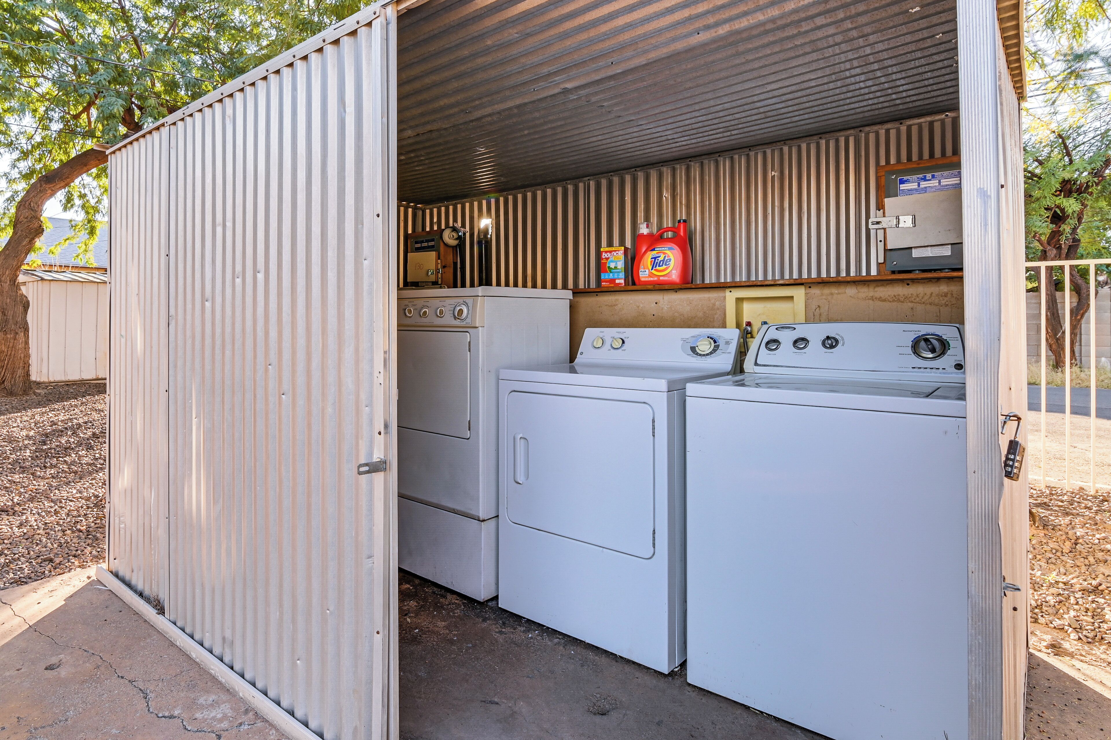 A compact laundry room with two washing machines and a dryer, equipped with a small shelf holding cleaning supplies.