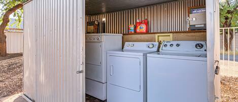 A compact laundry room with two washing machines and a dryer, equipped with a small shelf holding cleaning supplies.