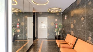 A modern lobby with a reception desk, a waiting area with orange seating, and circular ceiling lights. - Apts in a Condominium Just 550 Meters From Pereque Beach Etps (Porto Belo)