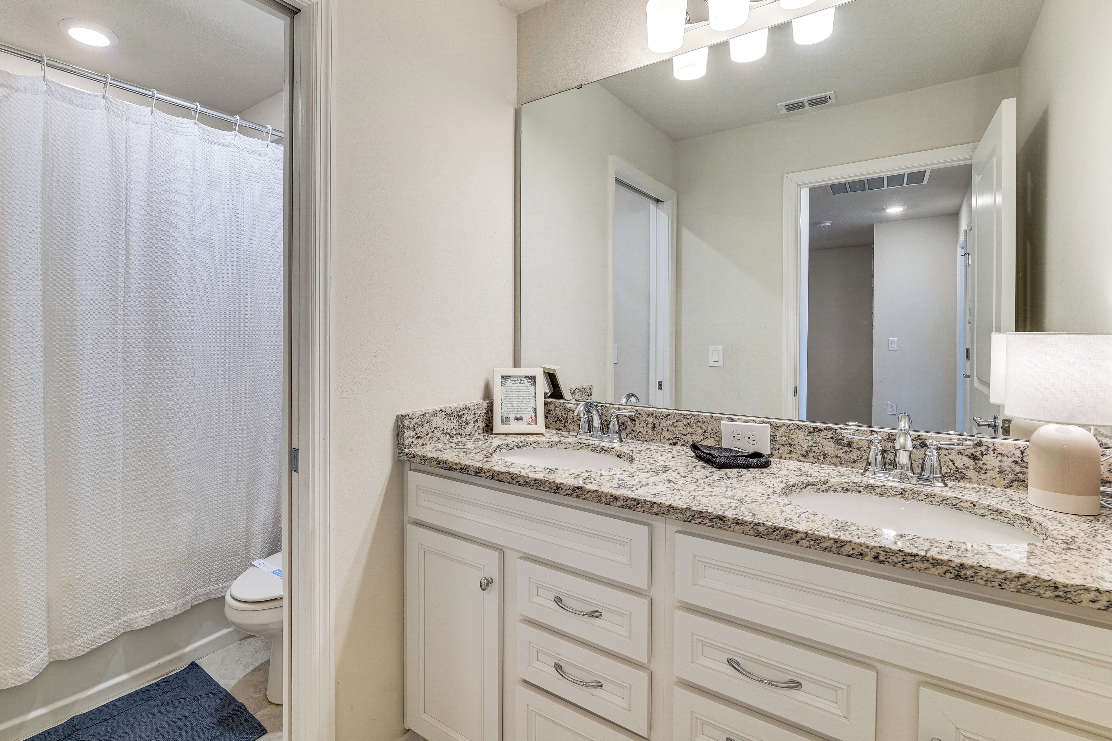 A bathroom with a granite countertop, a large mirror, and a white toilet.