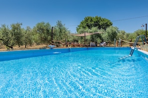 Una piscina cristallina circondata da sdraio di legno e un'area ombreggiata, con alberi sullo sfondo.
