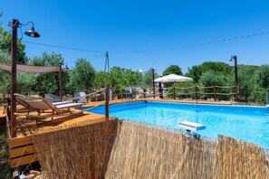 Ein Pool mit Liegestühlen und Sonnenschirmen, umgeben von einer Holzterrasse und einem Bambuszaun.