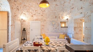 Una habitación con pared de piedra, cama con colcha de estampado geométrico, sofá blanco y una mesa con sillas.