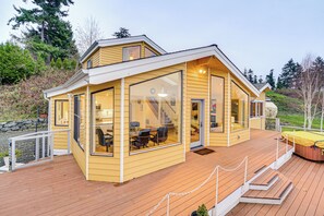 Uma cabana amarela com janelas amplas, um deck e uma banheira de hidromassagem.