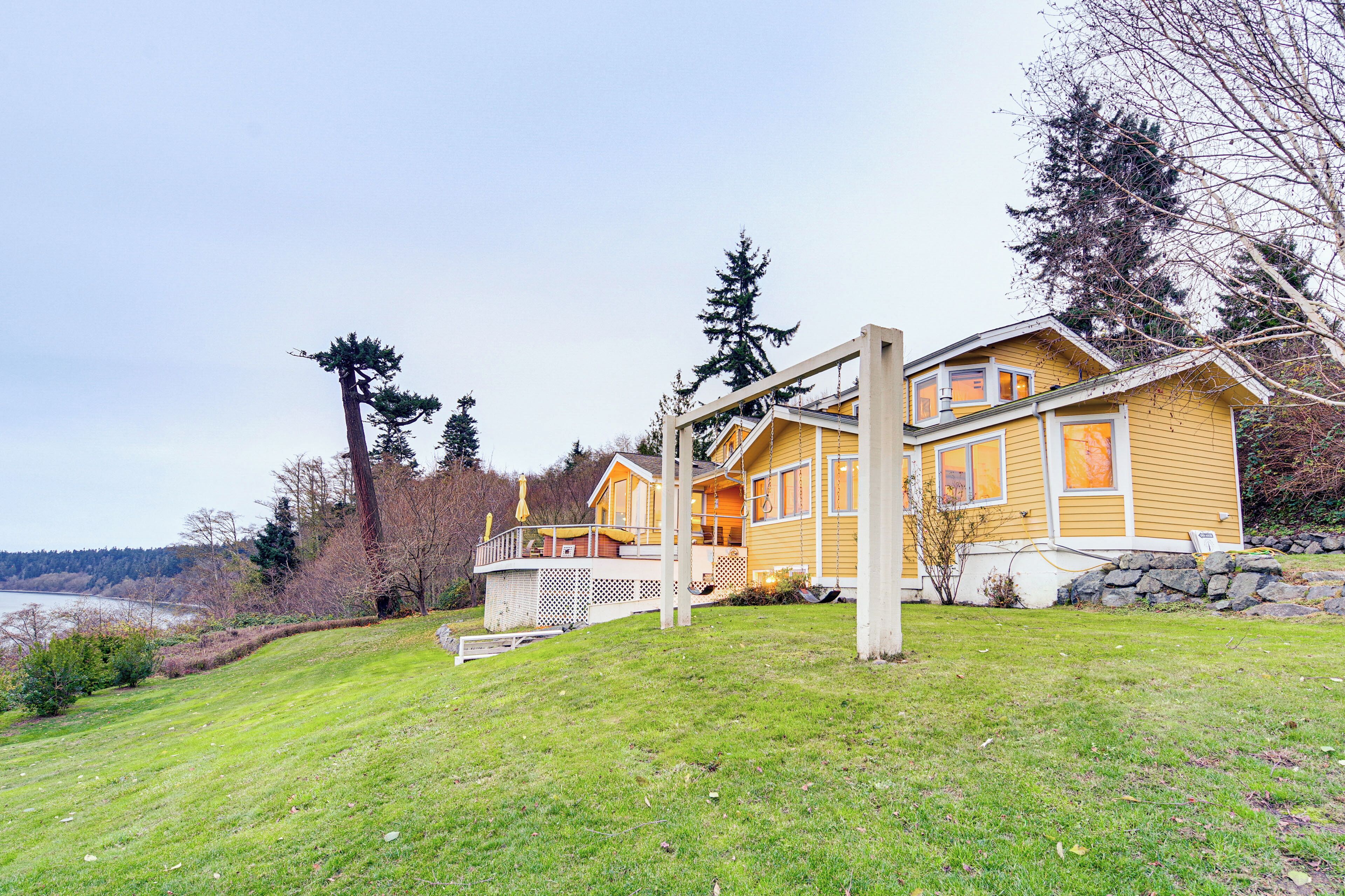 A two-story yellow house with a stone foundation, a wooden deck, and a view of a lake.
