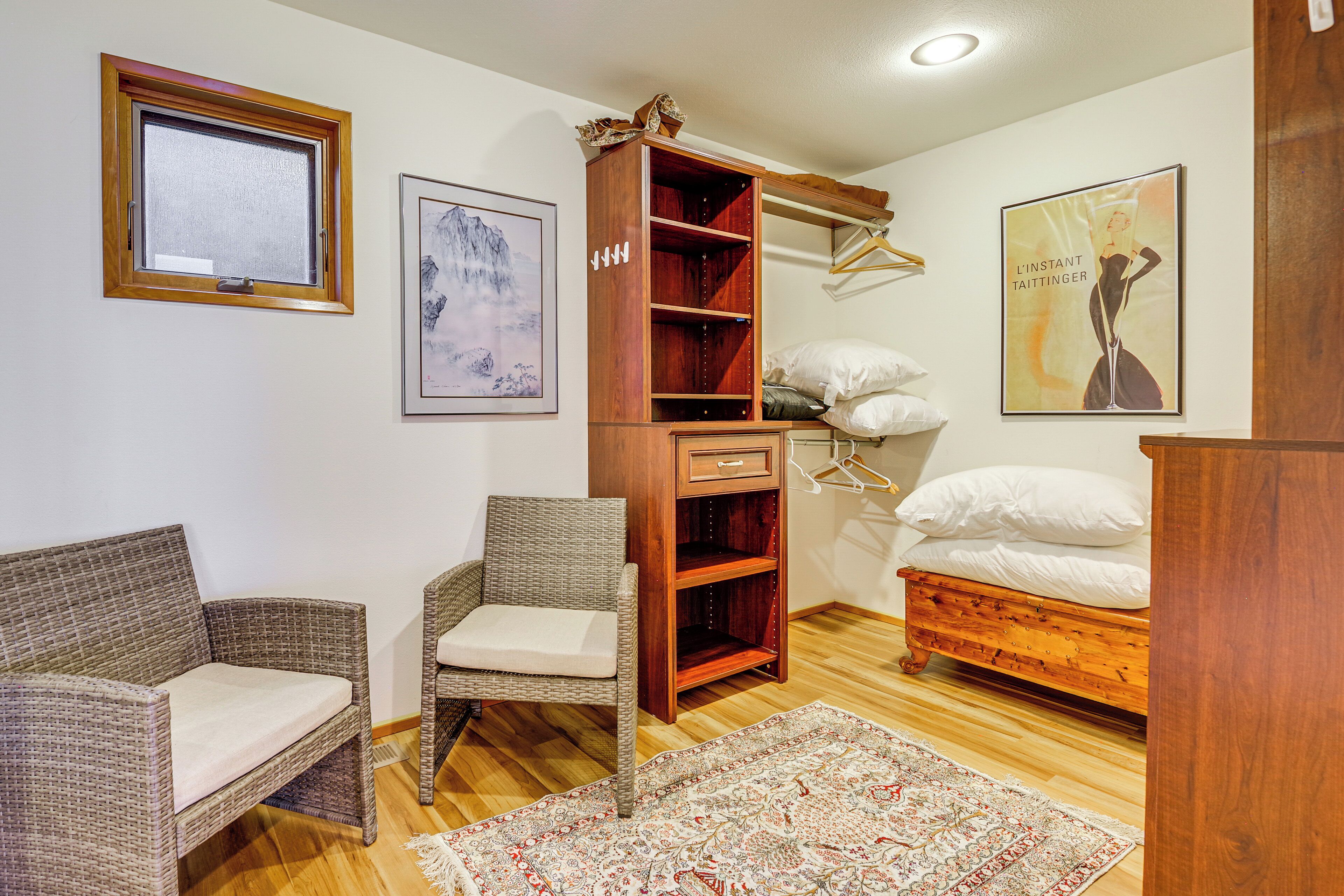 Ein Schlafzimmer mit einem hölzernen Bett, einem Korbstuhl, einem Holzschrank, einem gerahmten Bild an der Wand und einem gemusterten Teppich.