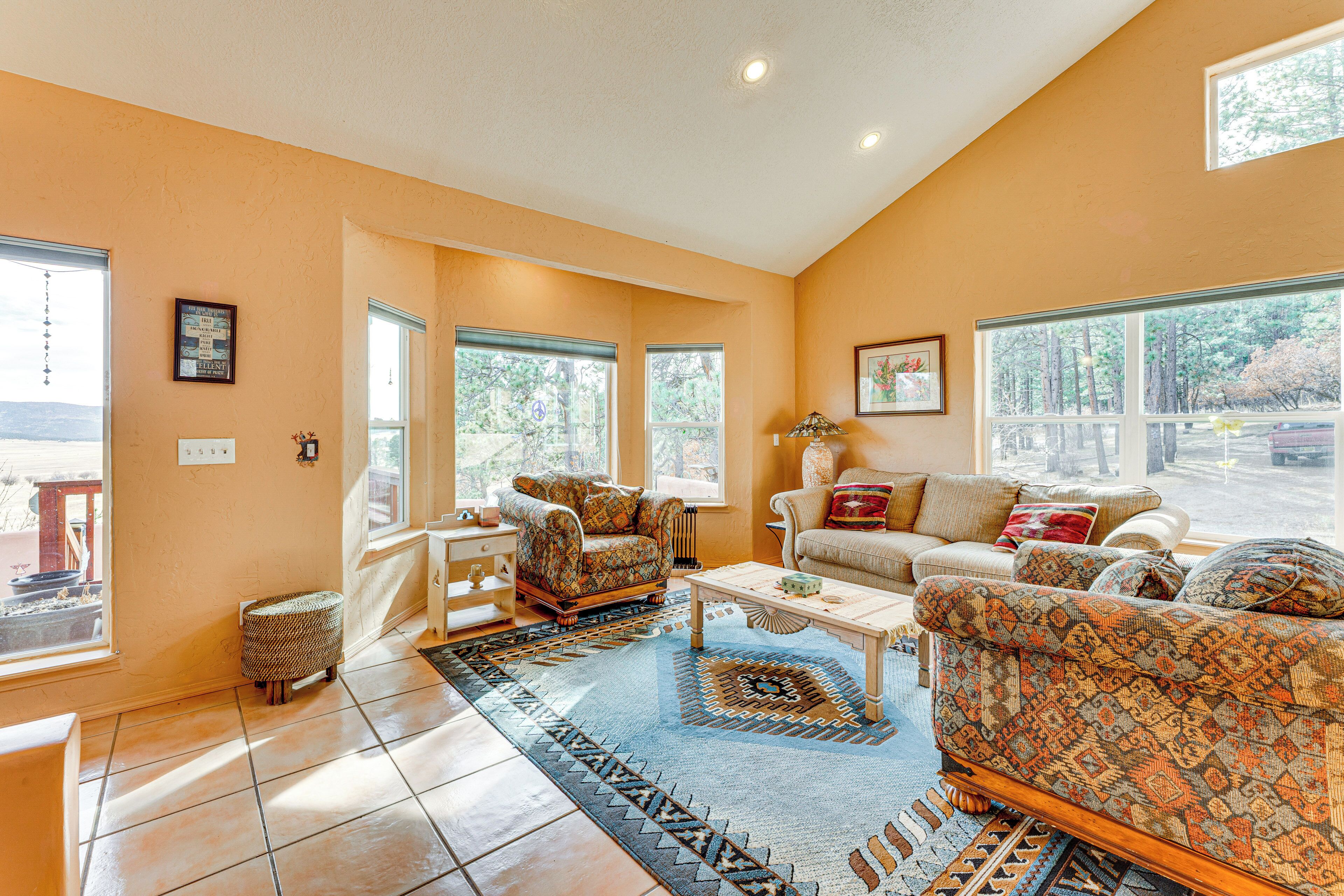 A spacious living room with large windows, a patterned sofa, a coffee table, and a patterned rug.