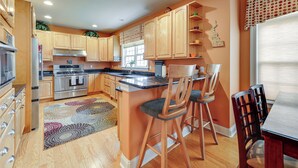 A modern kitchen with wooden cabinets, stainless steel appliances, and a bar area with stools. - 2 Mi to Bethany Beach! Spacious Family Retreat (Ocean View)