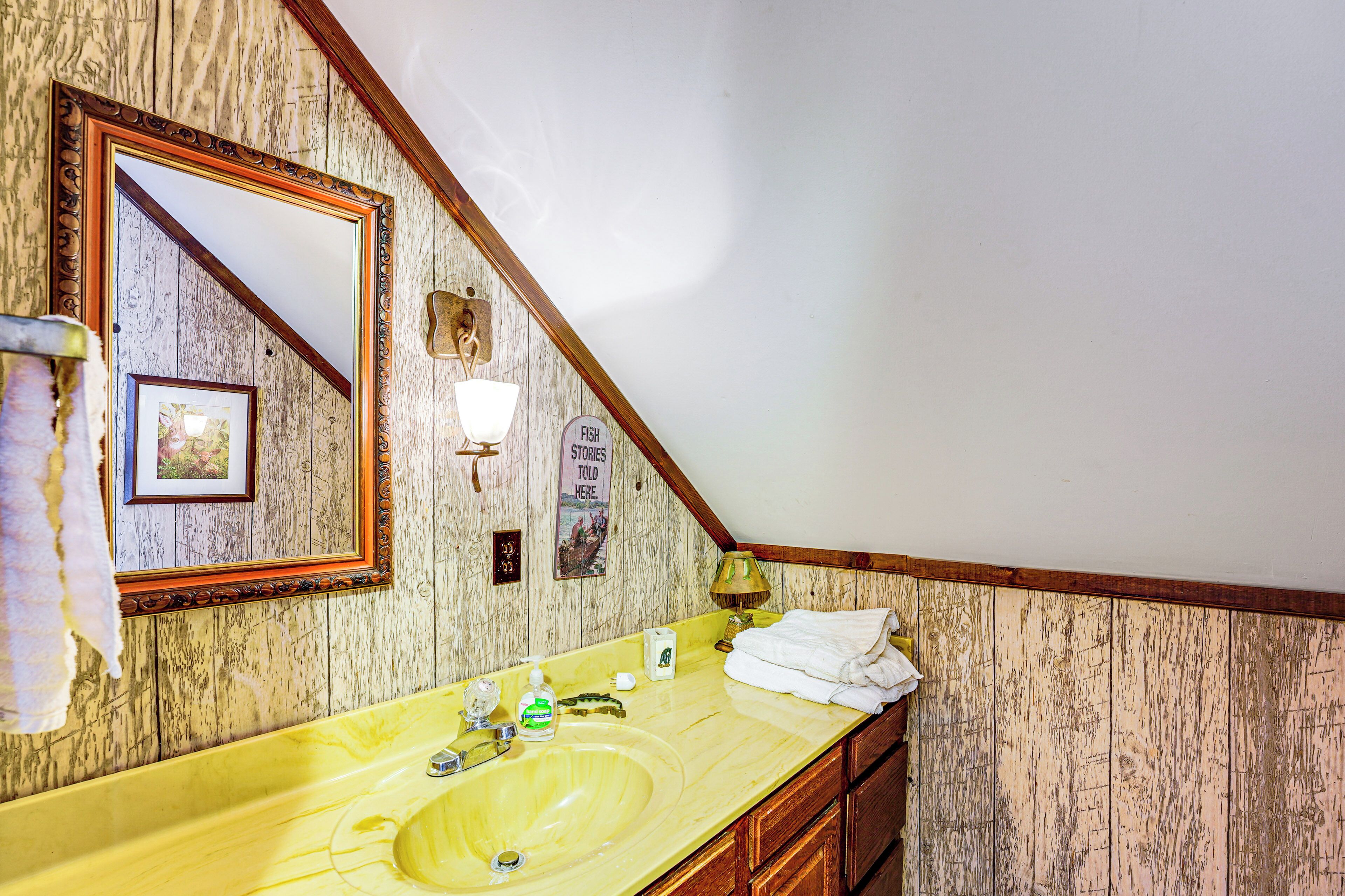 A bathroom with a wooden wall, a yellow sink, a mirror, a towel rack, and a sign that says "STORIES TOLD HERE."
