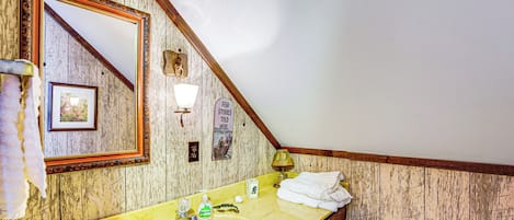 A bathroom with a wooden wall, a yellow sink, a mirror, a towel rack, and a sign that says "STORIES TOLD HERE."