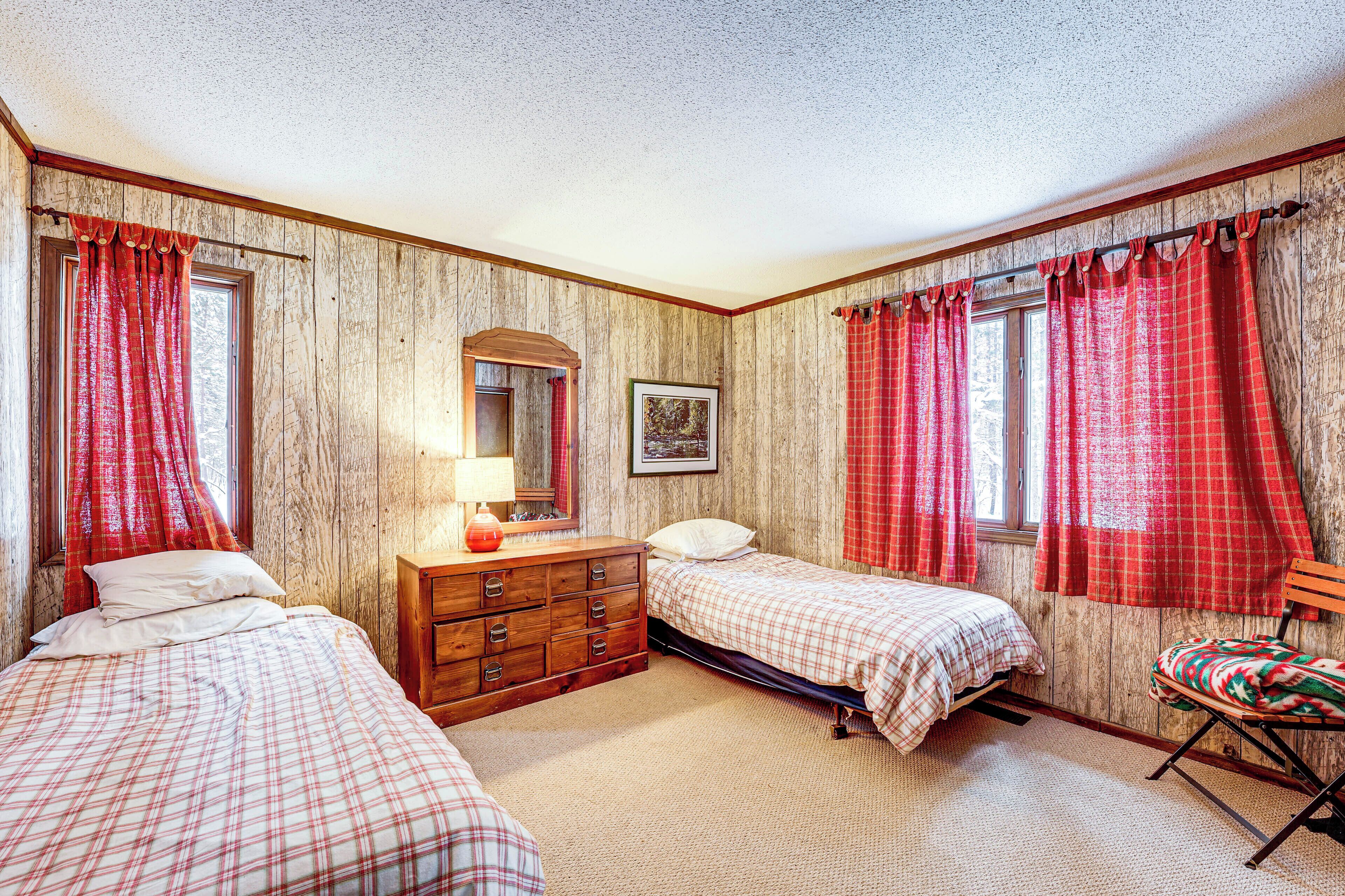 A bedroom with two beds, a dresser, a chair, and a window with red curtains.