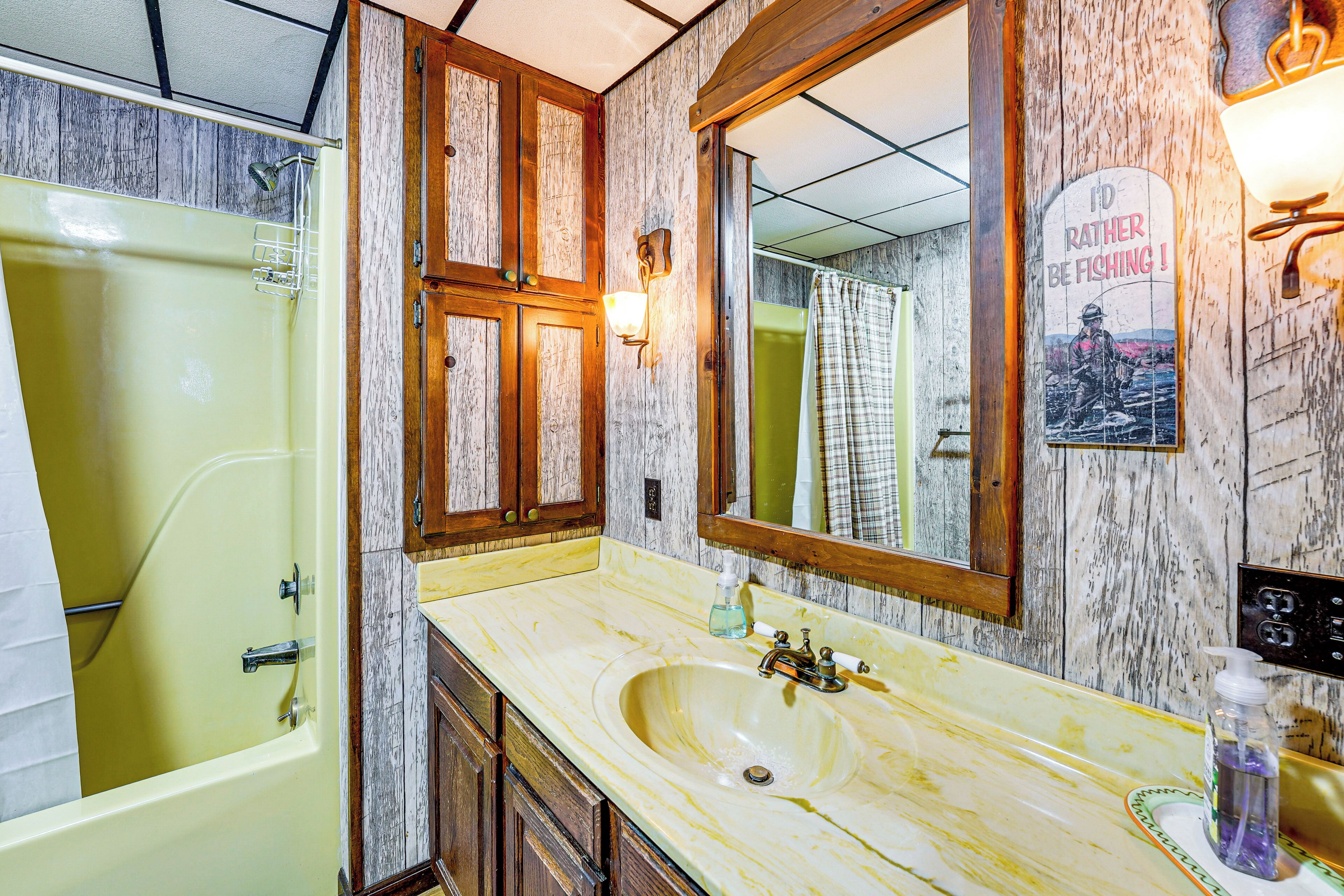 Une salle de bain avec une baignoire jaune, un lavabo avec un miroir au-dessus, des meubles en bois et une affiche accrochée au mur.