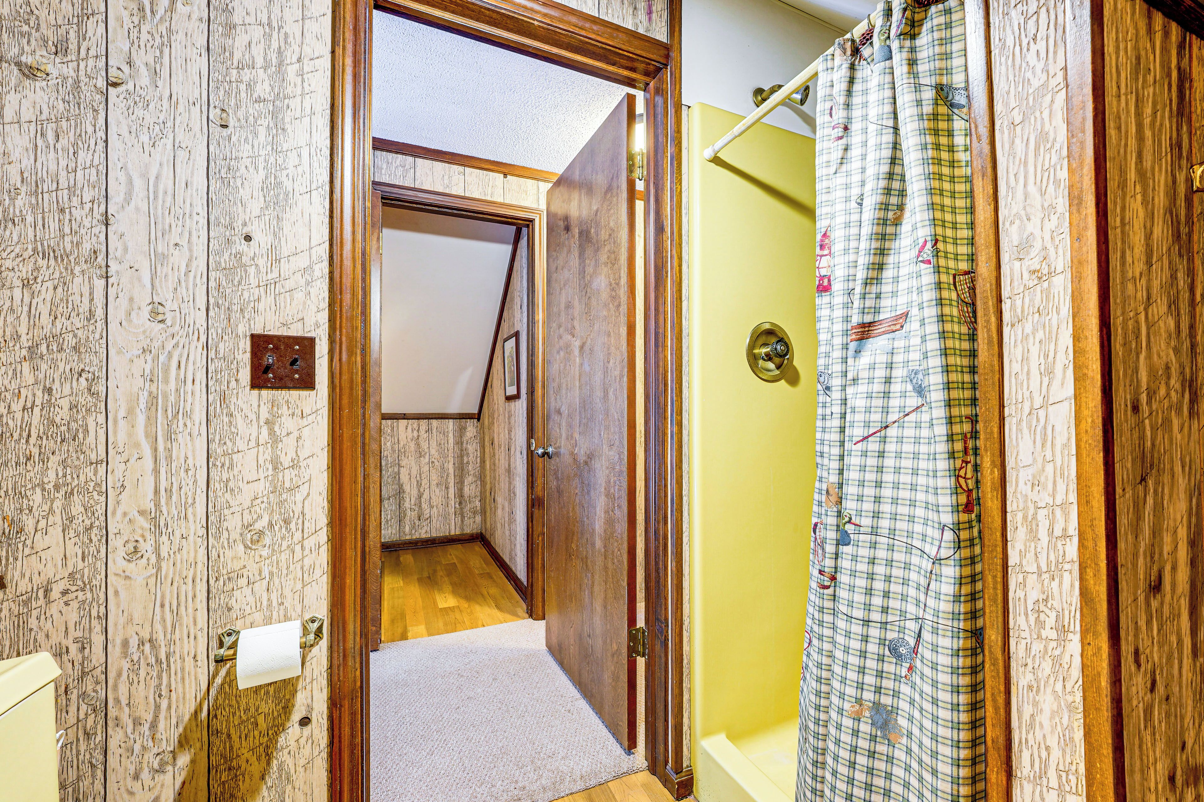 Un baño con puerta de madera, un perchero con un rollo de toallas de papel y una cortina de ducha estampada.